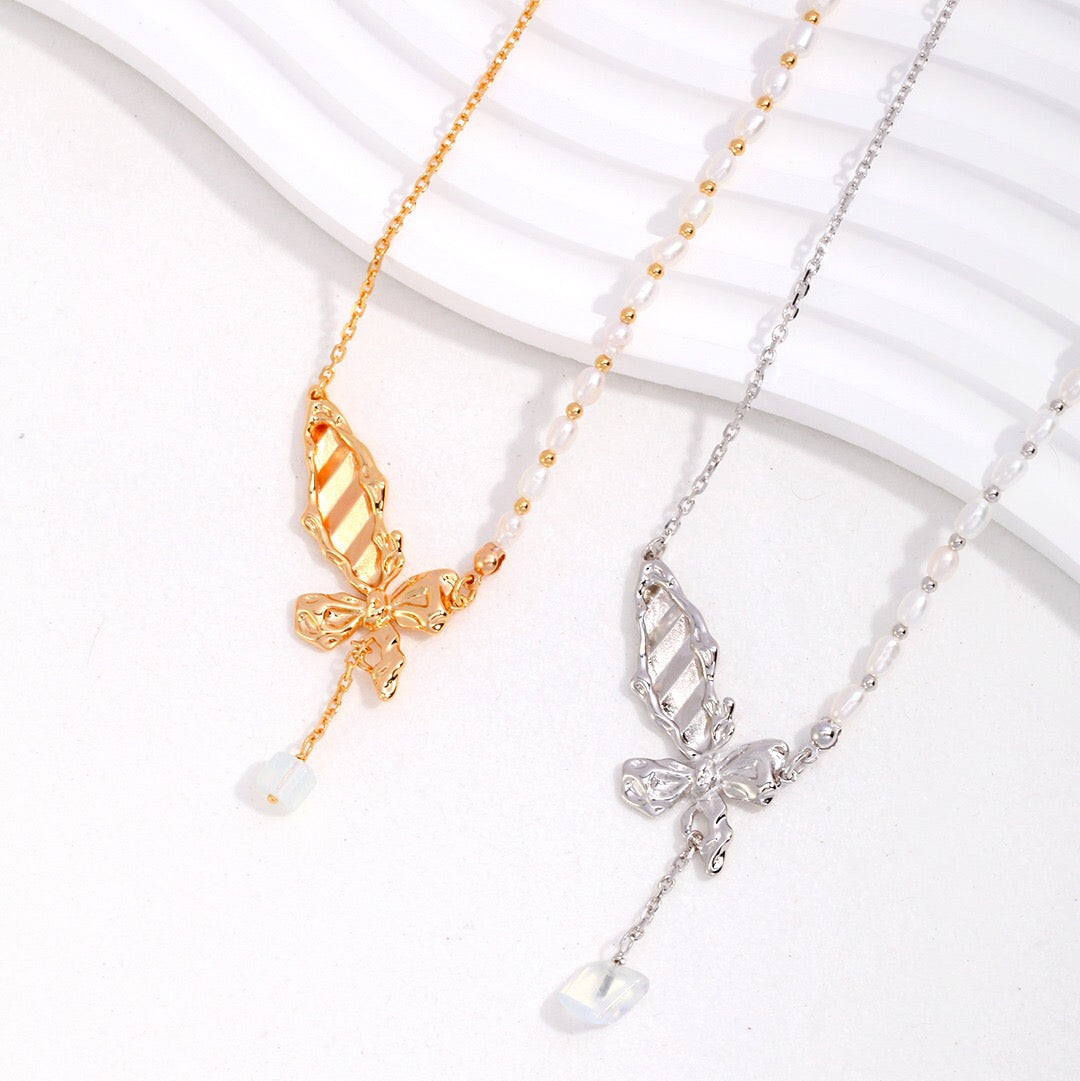 Two butterfly pearl necklaces, one with a gold vermeil butterfly and white pearl, the other with a silver butterfly and white pearl, displayed on a white surface.